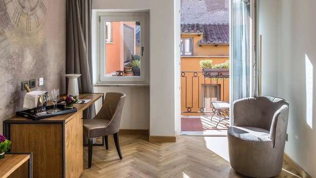 Une chambre moderne dotée d’un bureau en bois, d’une chaise, d’une grande fenêtre et d’un balcon offrant une vue sur le quartier.
