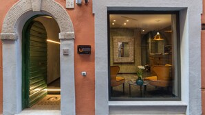 L’entrée d’un hôtel, avec une porte verte, une enseigne indiquant « NAVONA ESSENCE », et une vue sur l’intérieur, où l’on aperçoit un mur à motifs, un miroir et deux chaises.