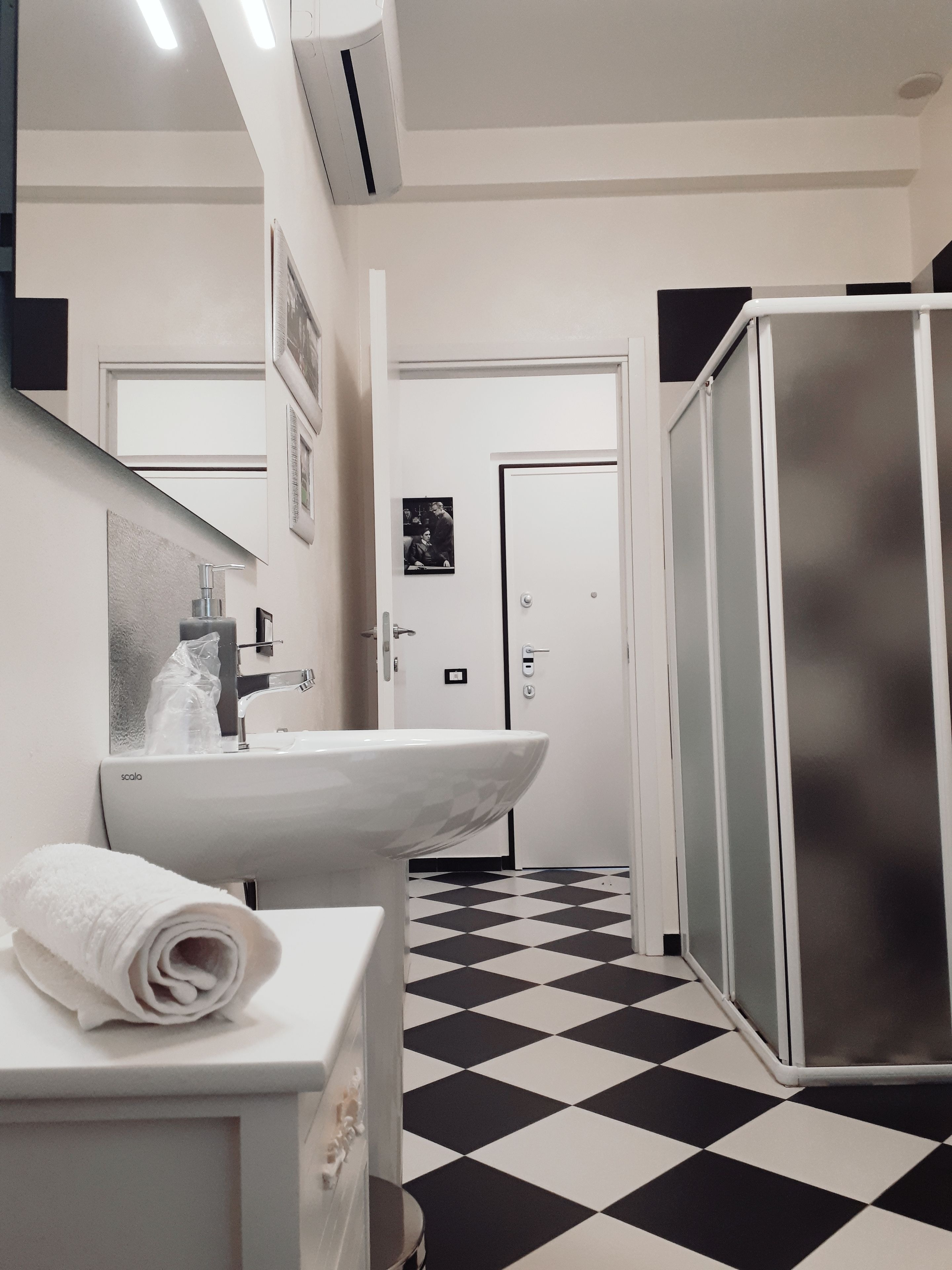 A bathroom with a white sink, a mirror, a towel, a shower, and a black and white checkered floor.