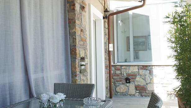 Un patio al aire libre con mobiliario de mimbre, una mesa de vidrio con flores y un muro de piedra.
