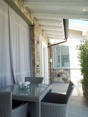 Une terrasse extérieure avec des meubles en osier, une table en verre ornée de fleurs et un mur en pierre.