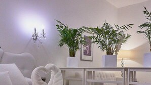 Una habitación de hotel con una cama bien tendida, un sofá blanco, una mesita y dos plantas en macetas.