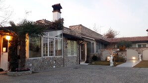 Una casa de piedra con un ventanal grande, una chimenea y un camino de entrada pavimentado.