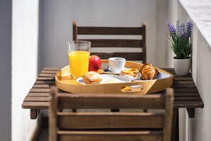 Una mesa de madera con una bandeja que contiene un croissant, un pastel, una manzana, un vaso de jugo de naranja y una taza.