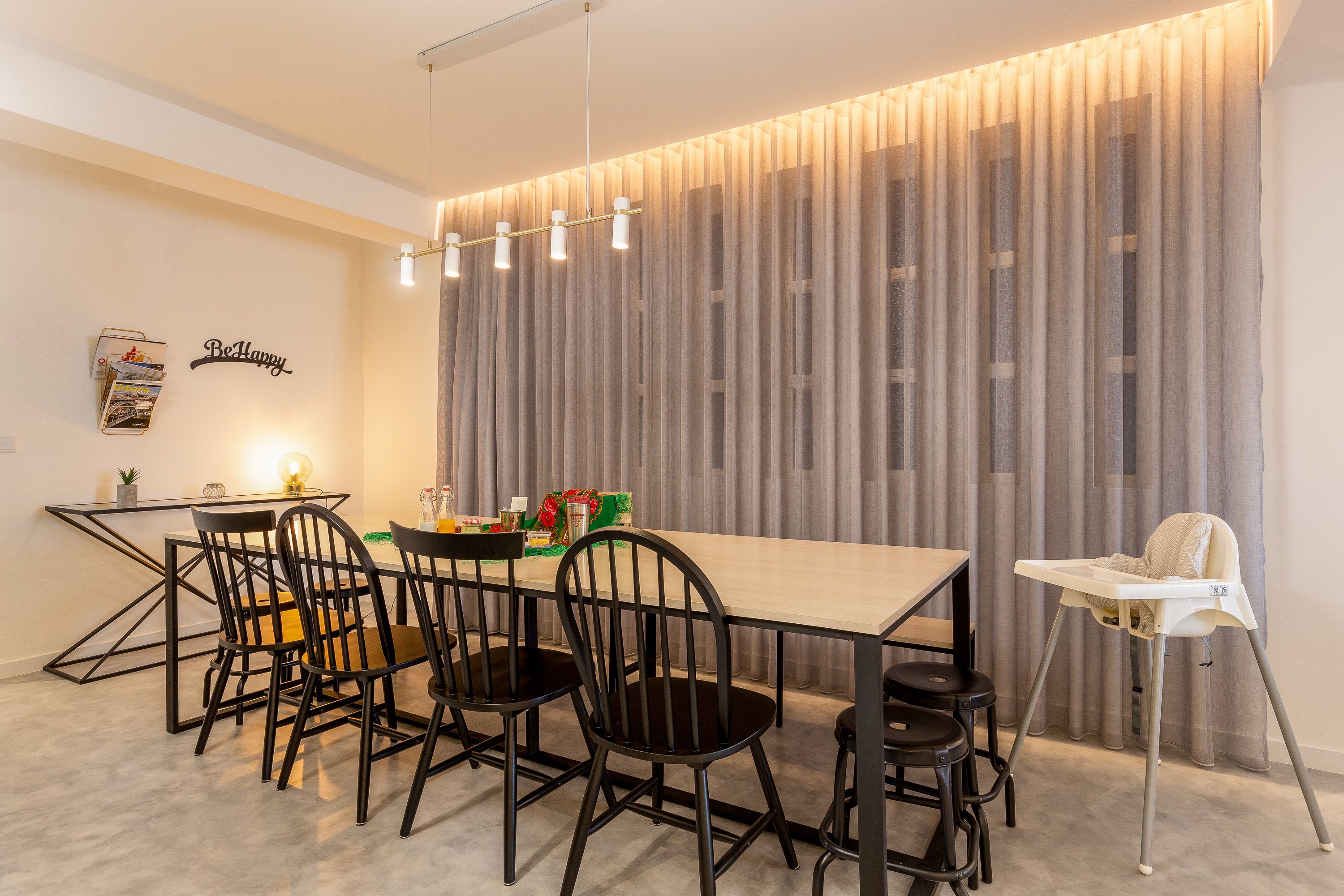 A modern dining area with a long table, black chairs, and a high chair.