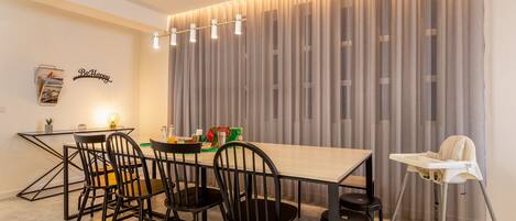 A modern dining area with a long table, black chairs, and a high chair.