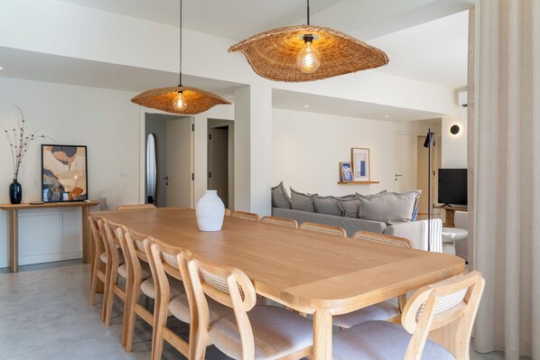 Un comedor amplio con una larga mesa de madera y sillas, dos lámparas colgantes tejidas y un diseño interior moderno.
