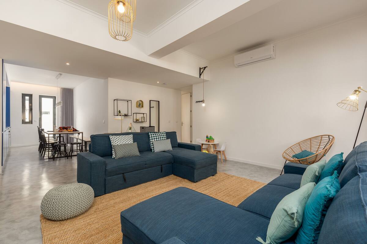 Una sala de estar moderna con un sofá modular, un comedor y una silla de mimbre.