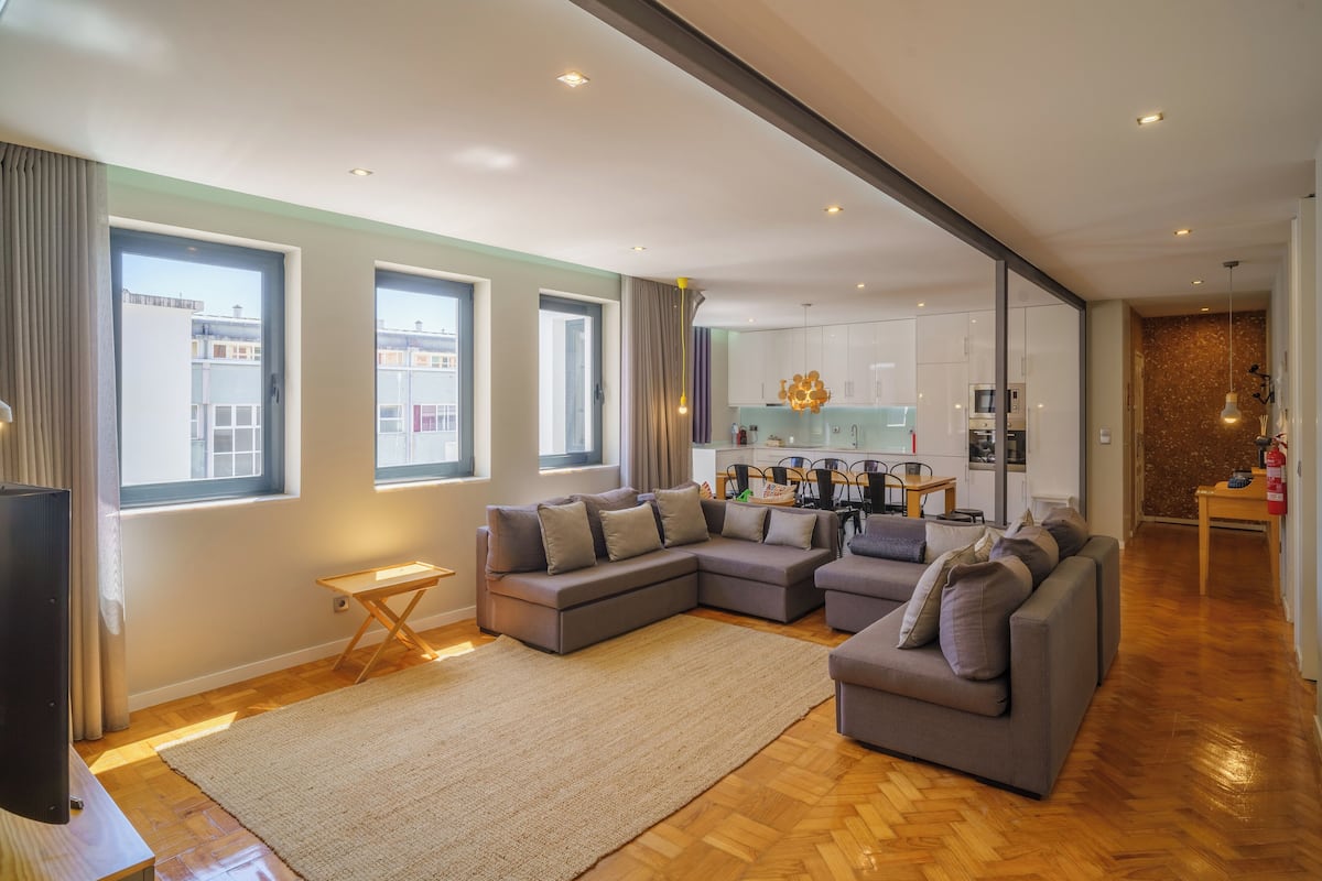 Una sala de estar moderna con un sofá modular, un televisor de pantalla plana y un comedor con una cocina al fondo.