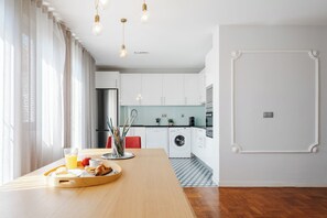 Cocina moderna con armarios blancos, lavadora y comedor con mesa de madera dispuesta para el desayuno.
