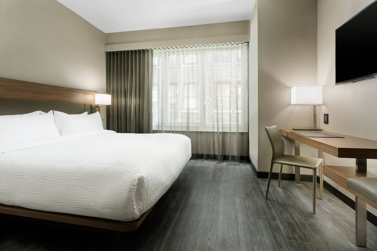 Een hotelkamer met een groot bed, een bureau met stoel, een televisie en een raam met gordijnen.