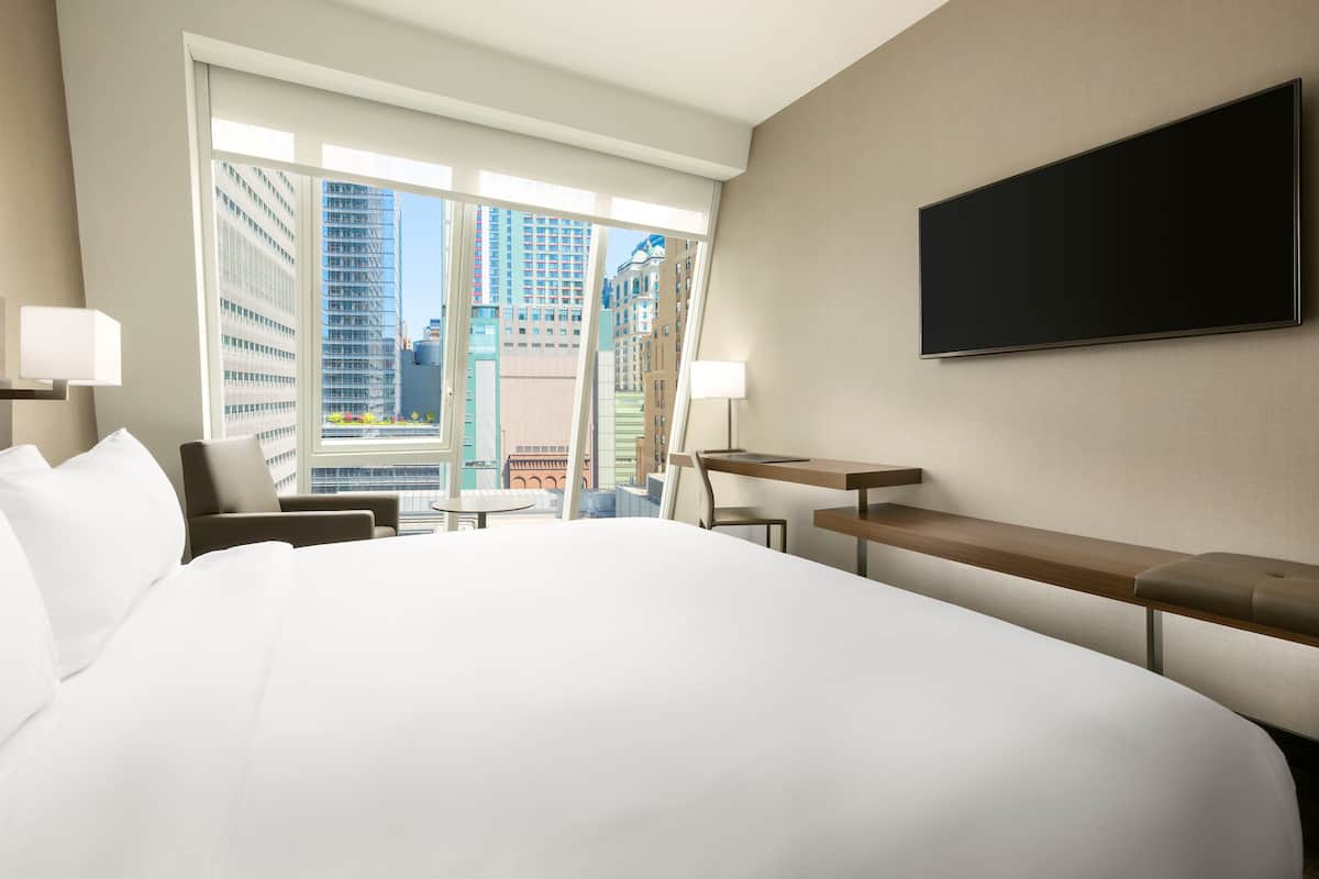 Een hotelkamer met een groot bed, een bureau, een stoel en een aan de muur bevestigde televisie.