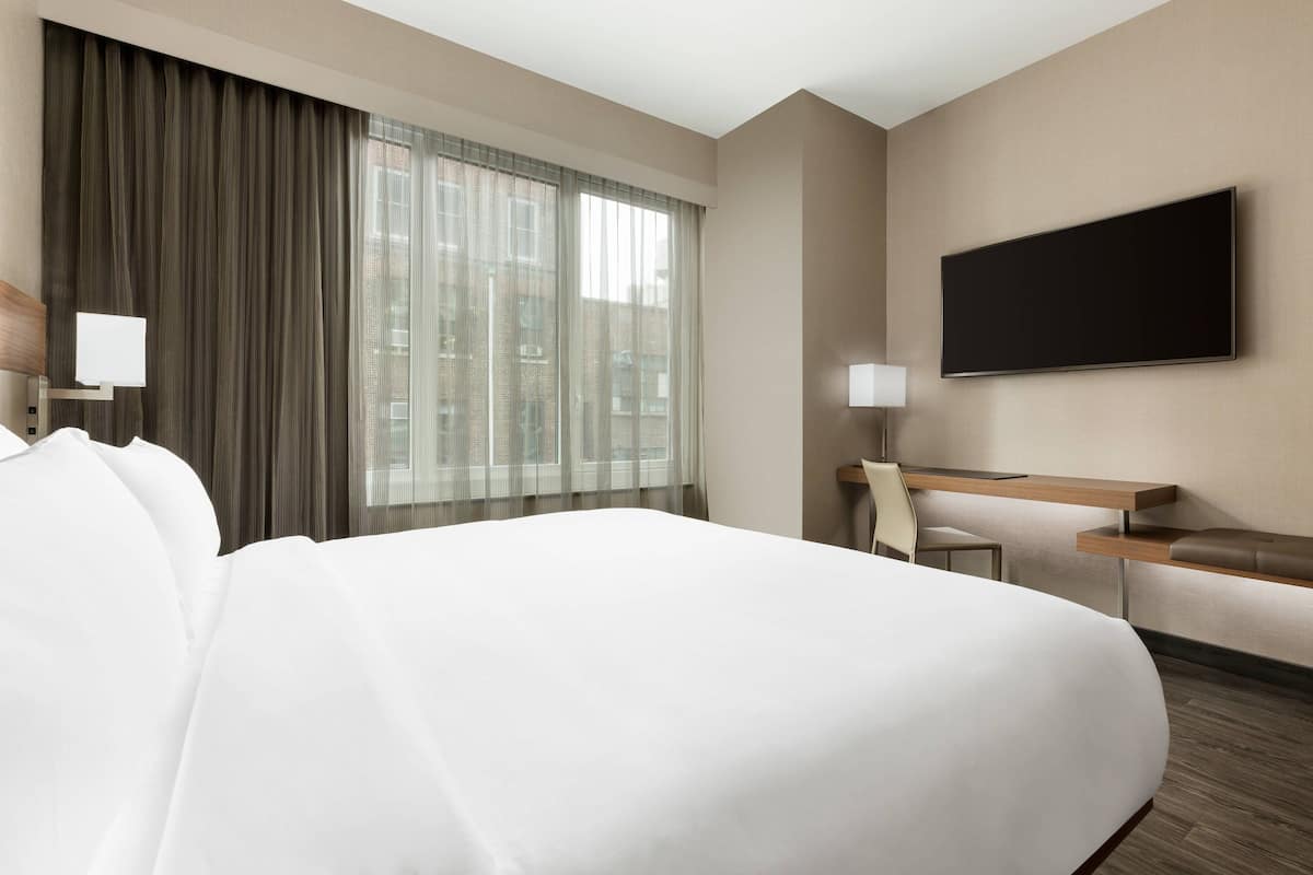 Een hotelkamer met een groot bed, een bureau met stoel, een flatscreen-tv aan de muur en een raam met gordijnen.