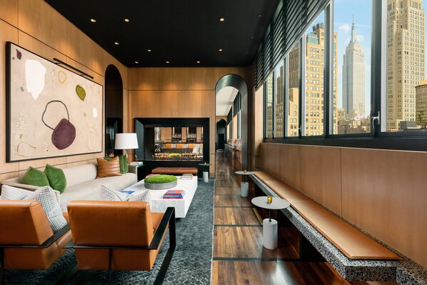 Un hall d’hôtel moderne avec un long banc, un espace salon et une vue sur l’Empire State Building.