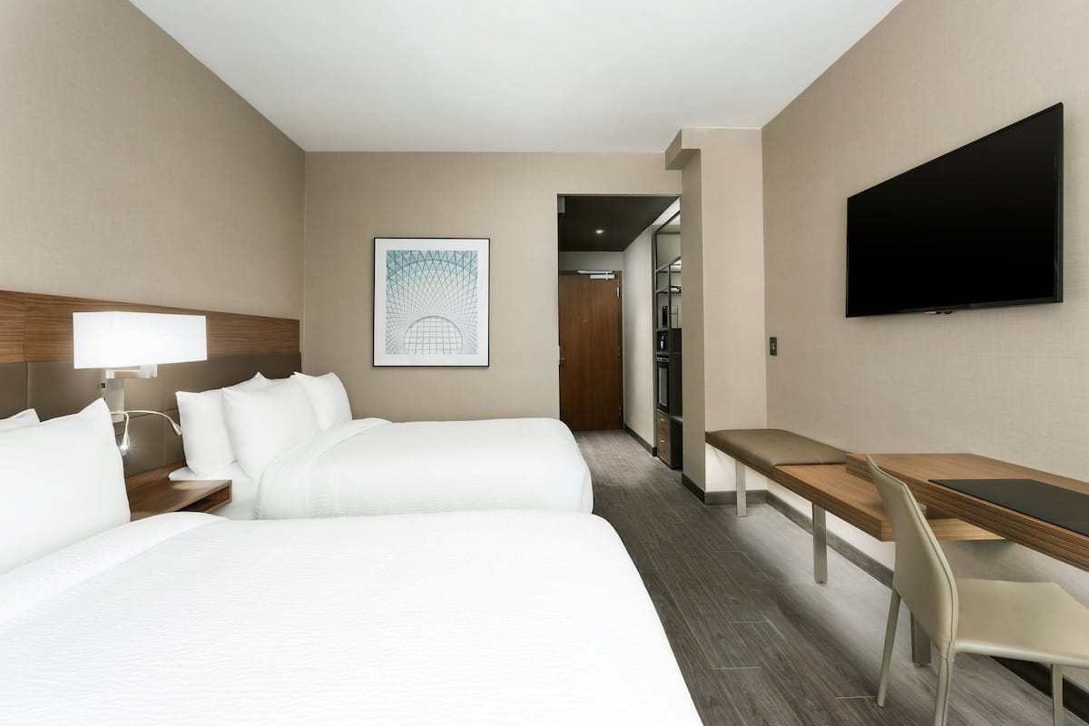 Hotelkamer met twee bedden, een bureau, een stoel, een flatscreen televisie en een kunstwerk in een lijst aan de muur.