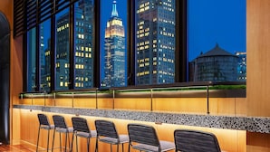 Un espace bar offrant une vue sur la ville, avec un design moderne, un comptoir en bois et des tabourets de bar.