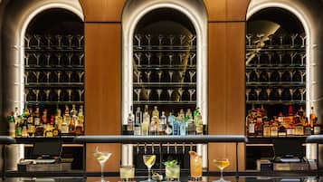A bar area with multiple shelves of liquor bottles, a cash register, and several glasses of drinks.