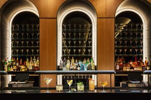 Un espace bar avec de nombreuses étagères remplies de bouteilles d’alcool, une caisse enregistreuse et plusieurs verres remplis de boissons.