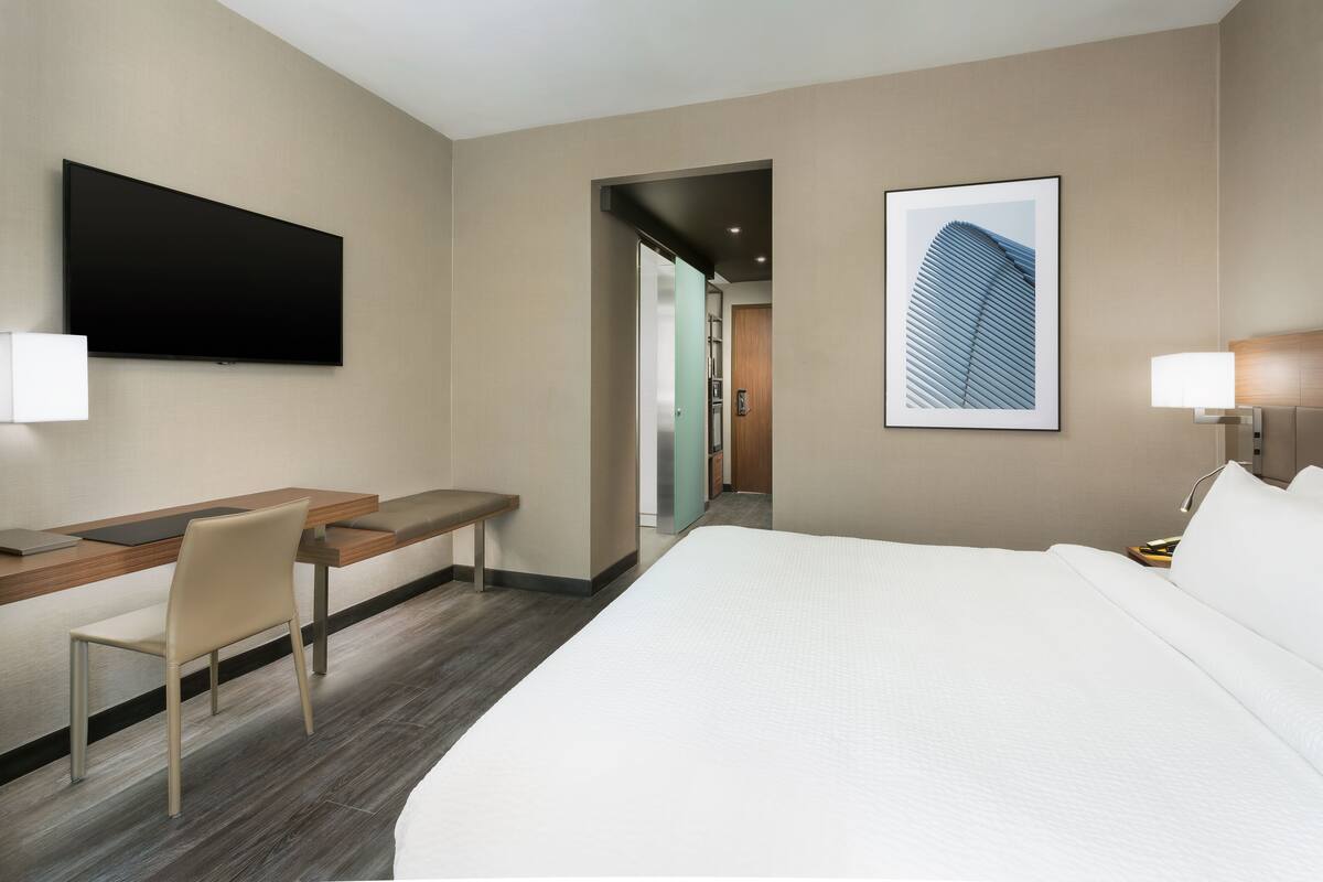 Hotelkamer met een groot bed, een bureau met stoel, een flatscreen televisie en een lijst met een afbeelding aan de muur.