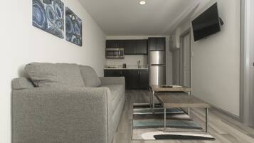 A modern kitchen with stainless steel appliances, a grey sofa, and a flat-screen TV mounted on the wall.