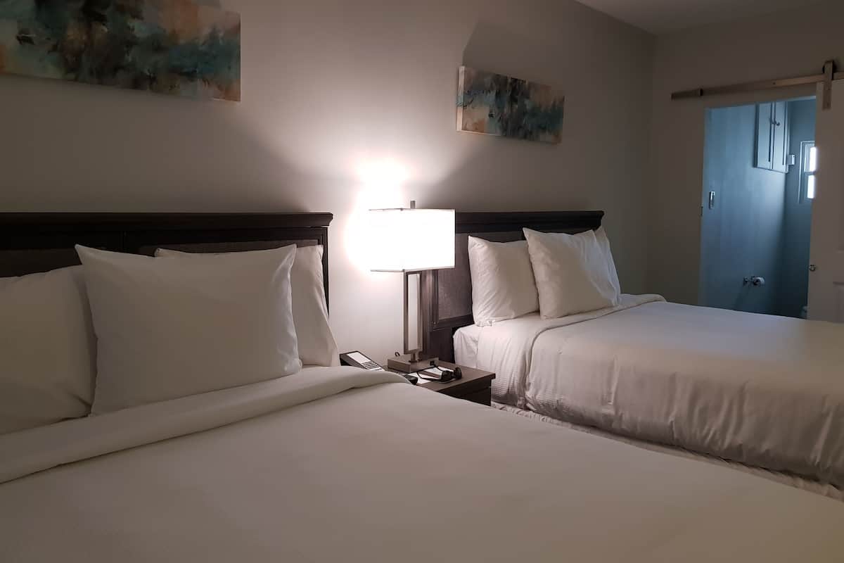 A hotel room with two beds, a nightstand with a lamp, and artwork on the walls.