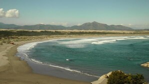 Un paisaje costero con playa, olas del océano y montañas lejanas bajo un cielo despejado.