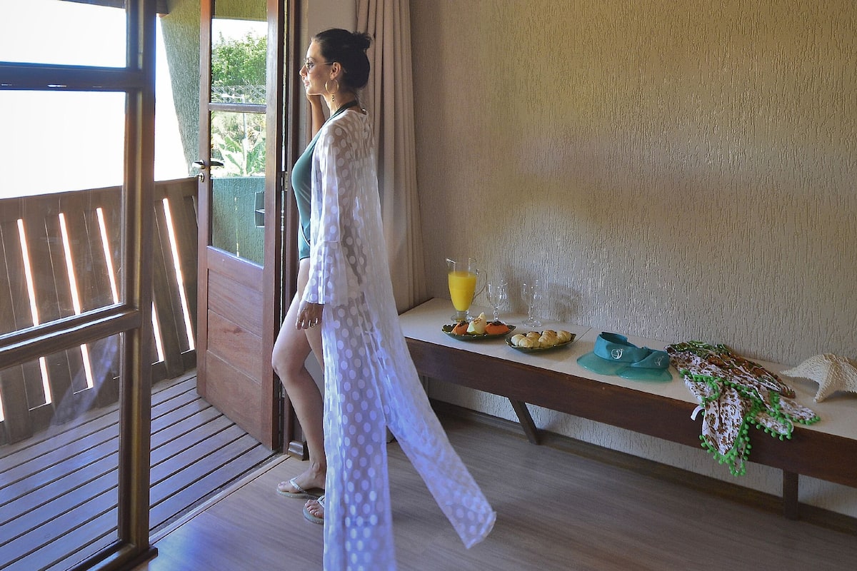 A balcony with a wooden railing, a table with food and drinks, and a person in a white dress.
