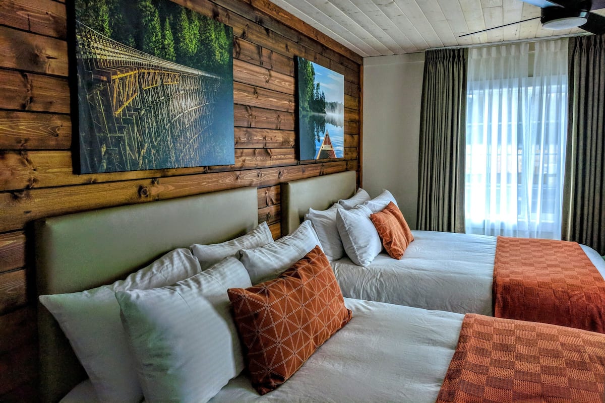 Habitación de hotel con dos camas, paneles de madera en las paredes y obras de arte que representan paisajes naturales.