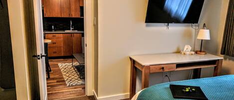 A hotel room with a bed, a desk, a TV, and a kitchenette.