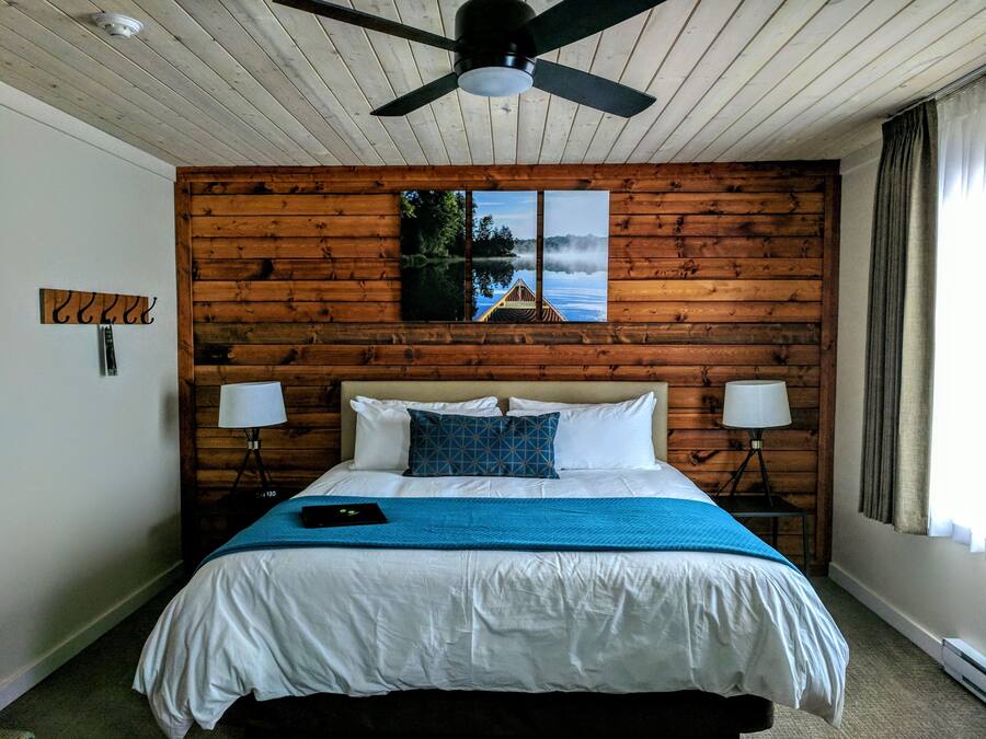 Una camera da letto con una testiera in legno, un letto con biancheria da letto bianca e una coperta blu, due abat-jour e una ventola a soffitto.