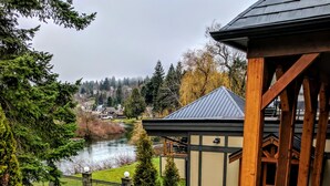 A covered outdoor area with a stone patio, a wooden pergola, and a view of a river and houses in the background. - Riverside Inn (Lake Cowichan)