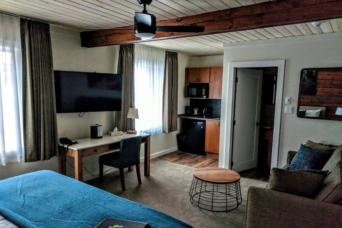 Habitación de hotel con cama, escritorio, silla, kitchenette y televisor.