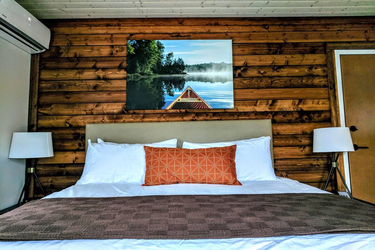 Habitación con paneles de madera, una cama, dos lámparas de noche y un cuadro con una vista de un lago.