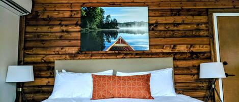 Habitación con paneles de madera, una cama, dos lámparas de noche y un cuadro con una vista de un lago.
