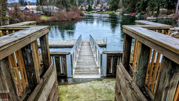 A wooden staircase leading to a dock over a calm river, surrounded by trees and houses. - Riverside Inn (Lake Cowichan)