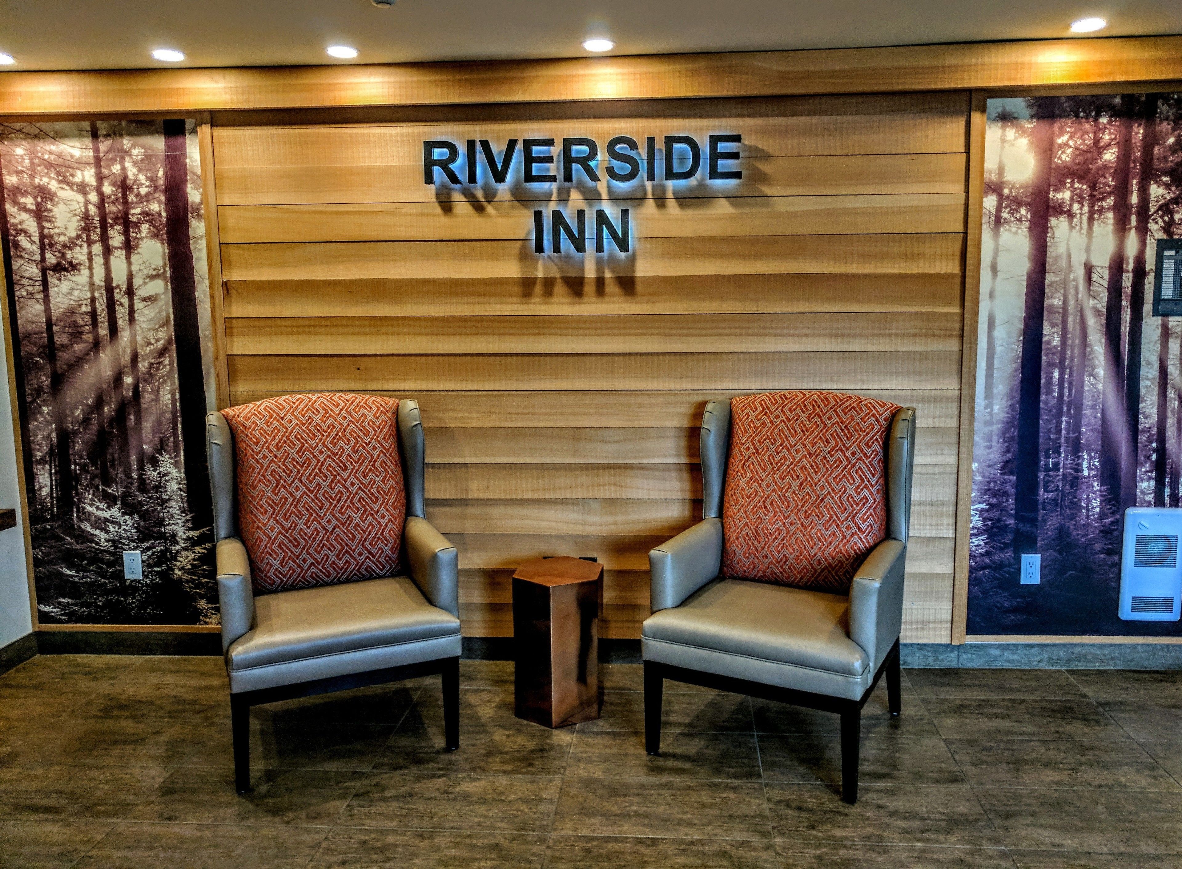 A reception area with two armchairs, a wooden wall with the name "Riverside Inn" illuminated, and forest-themed wallpaper on either side.