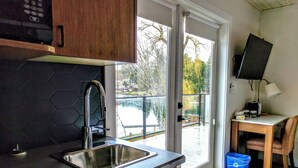 A kitchen with a stainless steel sink, wooden cabinets, and a view of a lake through the sliding glass door. - Riverside Inn (Lake Cowichan)