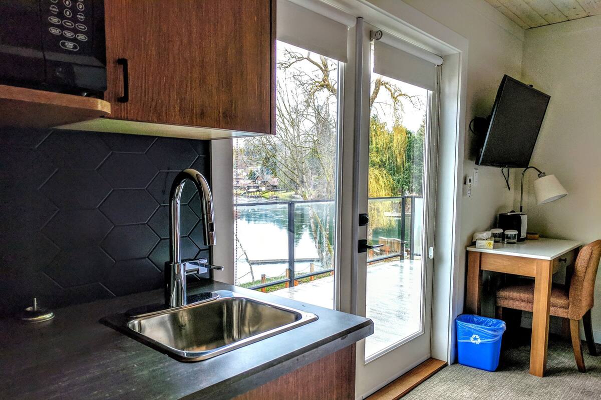 Una cocina con un lavamanos de acero inoxidable, armarios de madera y vista a un lago a través de una puerta corrediza de vidrio.
