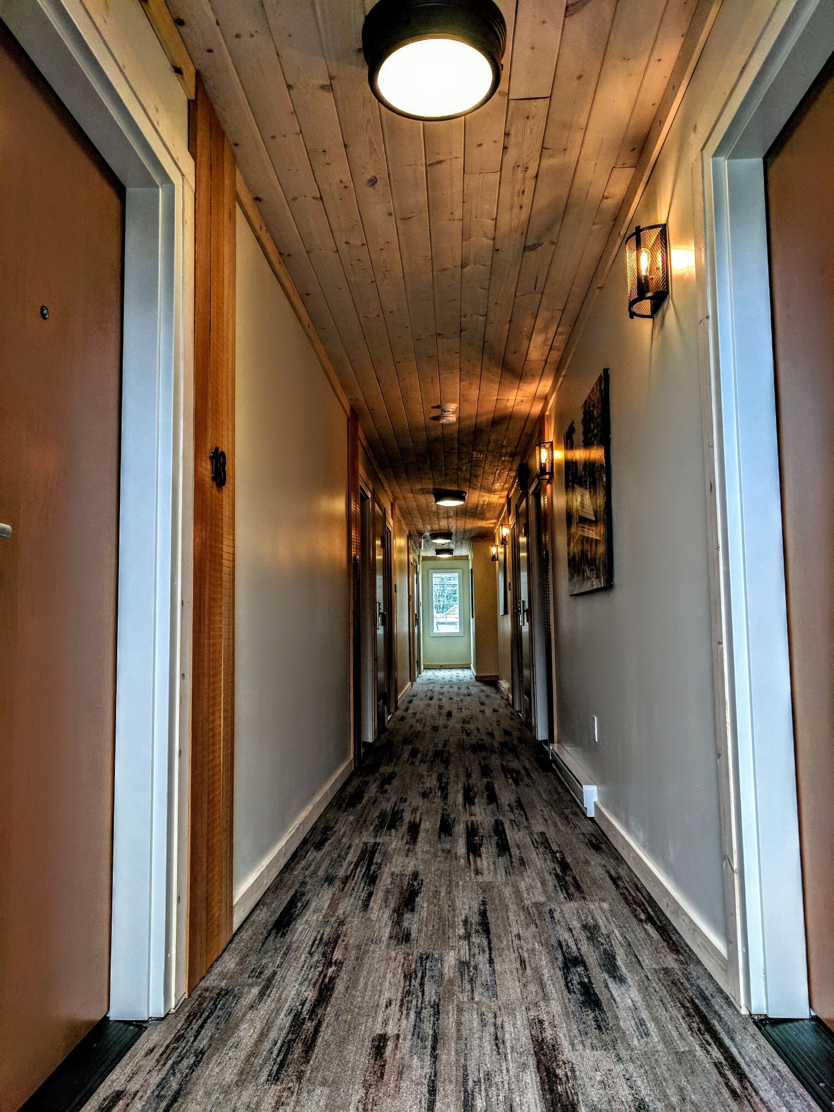 A long, narrow hallway with wooden panel ceilings and a carpeted floor.