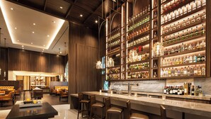 A bar area with a long counter, multiple stools, and shelves stocked with various bottles. - Sheraton Los Angeles San Gabriel (San Gabriel)