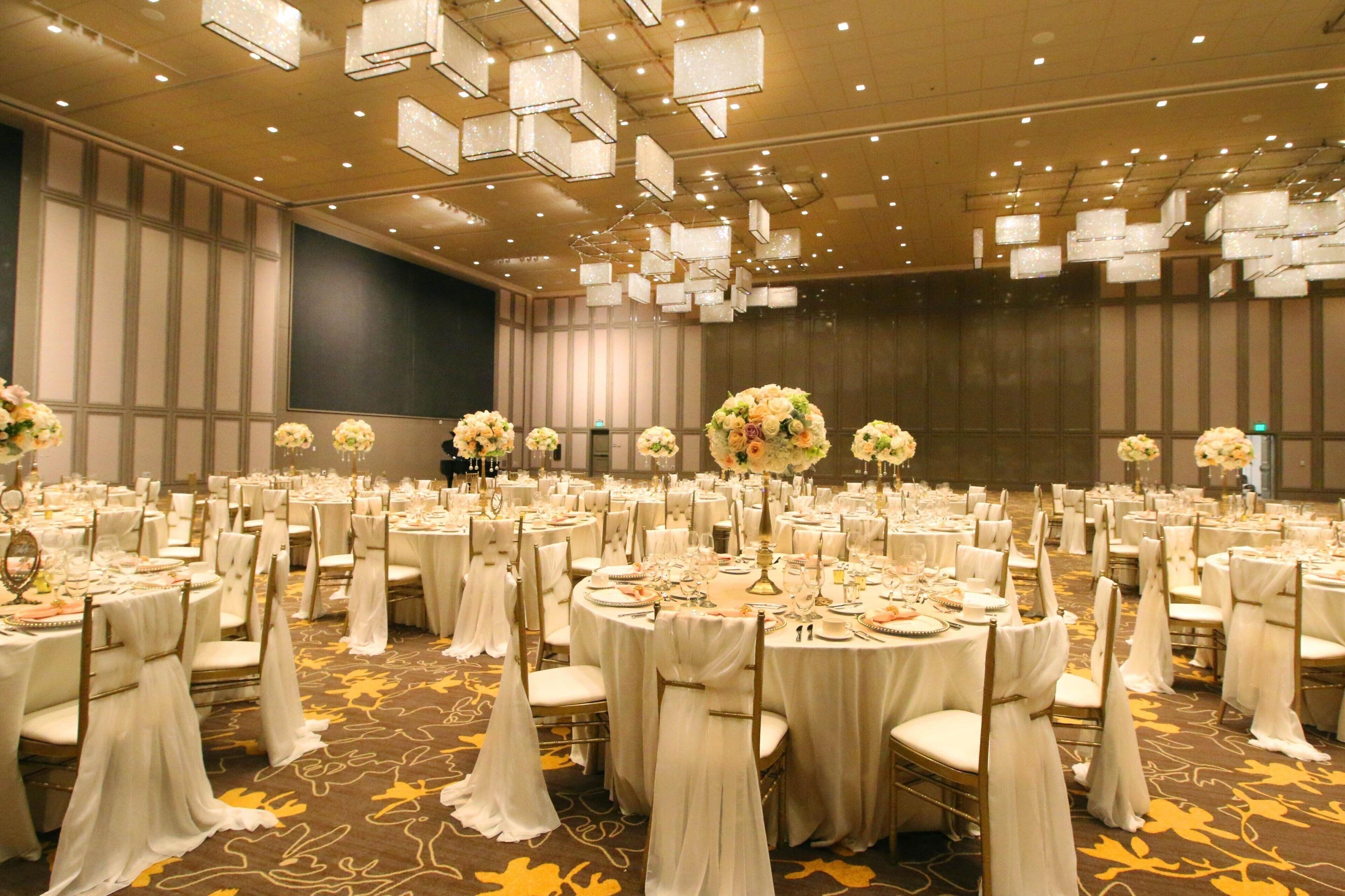 A banquet hall with round tables, white tablecloths, and floral centerpieces.