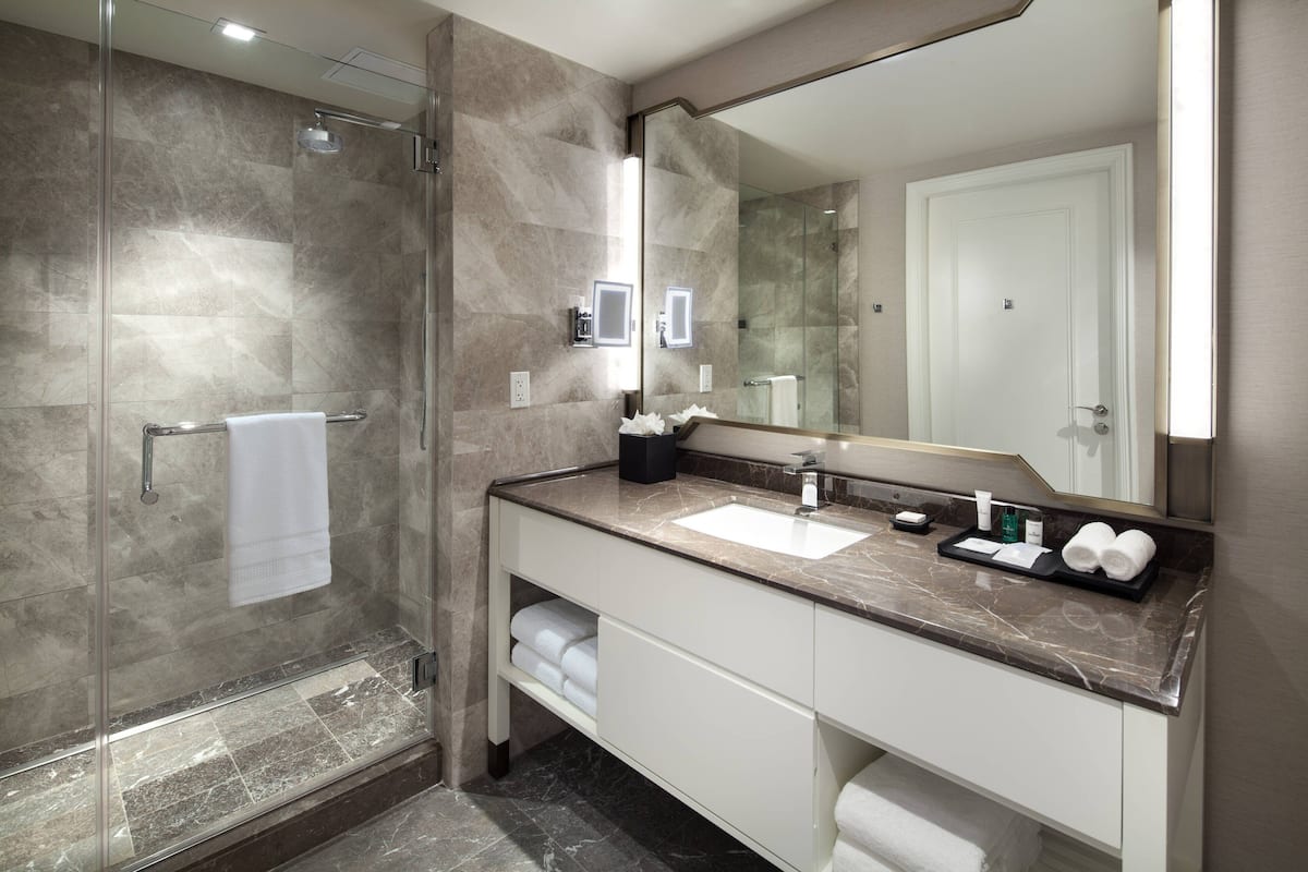 Een moderne badkamer met een douche met glazen wand, een grote spiegel en een marmeren aanrechtblad.