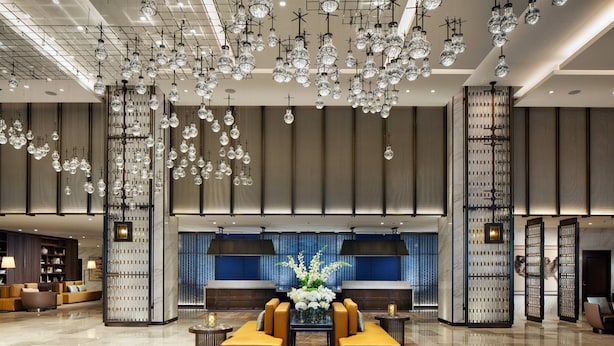 A spacious lobby with a modern chandelier, seating area, and a decorative wall with a blue backdrop. - Sheraton Los Angeles San Gabriel (San Gabriel)