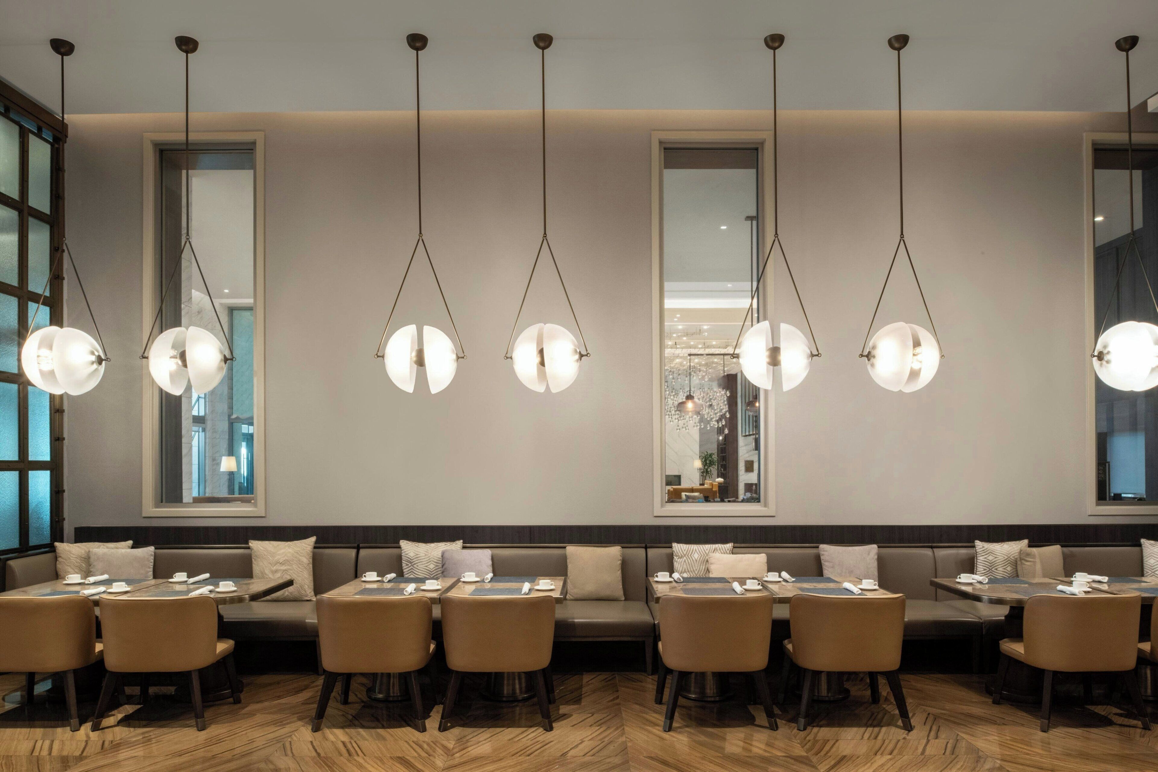 Un restaurante moderno con una barra alargada, varias zonas de estar e iluminación colgante.