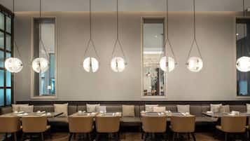 Un restaurante moderno con una barra alargada, varias zonas de estar e iluminación colgante.