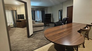 Habitación de hotel con una mesa de comedor de madera, un sofá, un televisor y un escritorio.