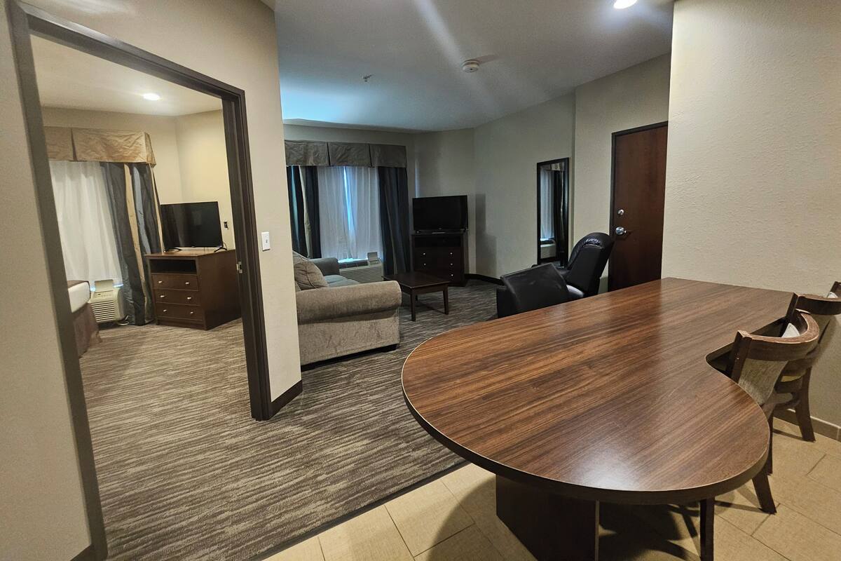 Une chambre d’hôtel avec une table à manger en bois, un canapé, une télévision et un bureau.