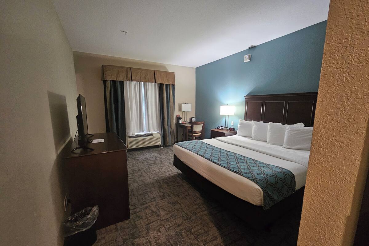 Une chambre d’hôtel avec un grand lit, un bureau avec un ordinateur, une lampe et une fenêtre avec des rideaux.