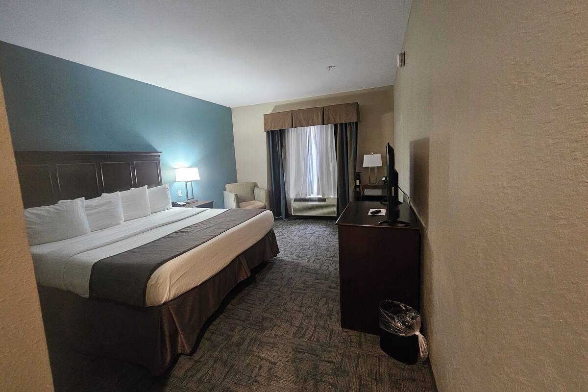 Une chambre d’hôtel avec un grand lit, un bureau avec une télévision, une chaise et une fenêtre avec des rideaux.