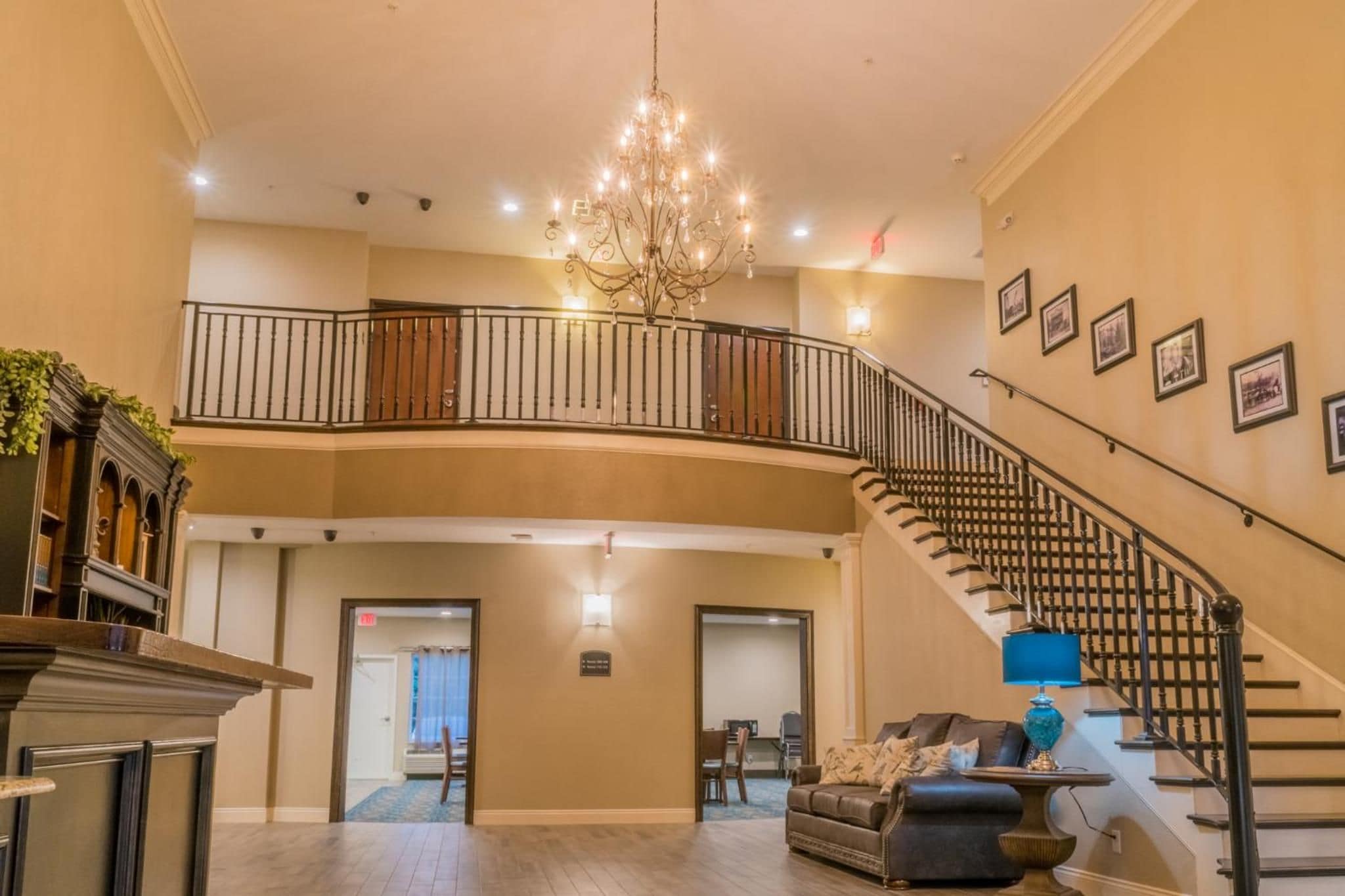 A spacious lobby with a grand staircase, a chandelier, and framed pictures on the walls.